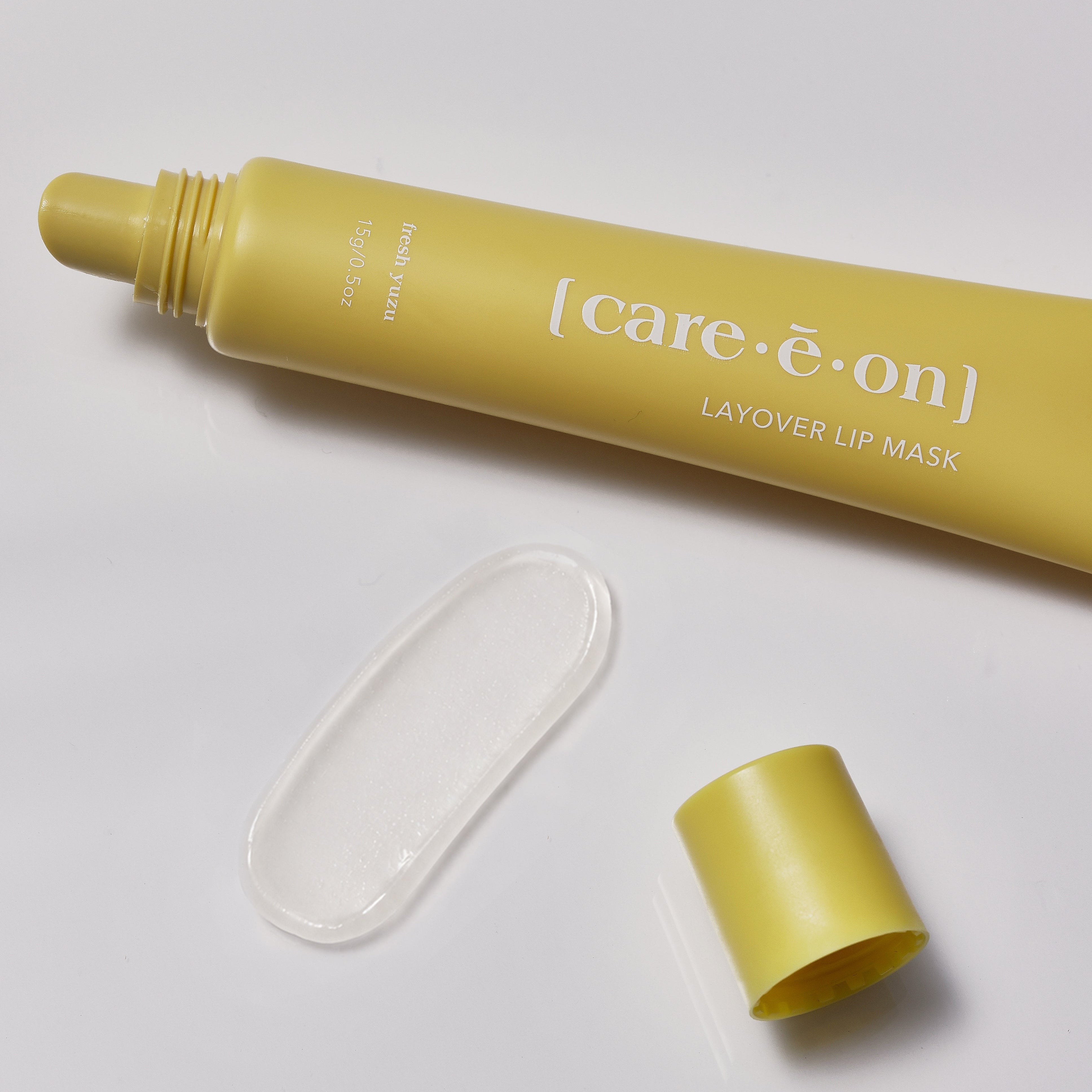 A yellow squeeze tube of [care·e·on] Layover Lip Mask with its protective cap and yellow applicator tip placed beside it on a clean white background.