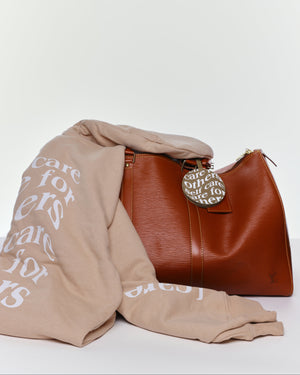 Care.ē.on En Route Hoodie folded beside a travel bag and luggage tag.