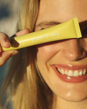 Woman holding the Care.ē.on Layover Lip Mask while smiling.