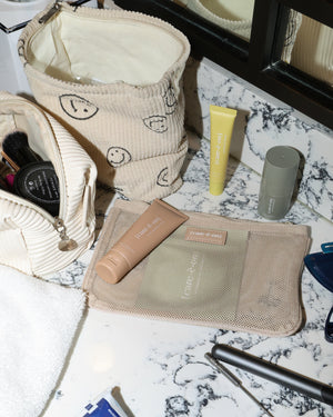 Care.ē.on travel skincare products, including the Flying Highdration Mask, Layover Lip Mask, and In the Clouds Mist, arranged with toiletry bags on a bathroom counter.